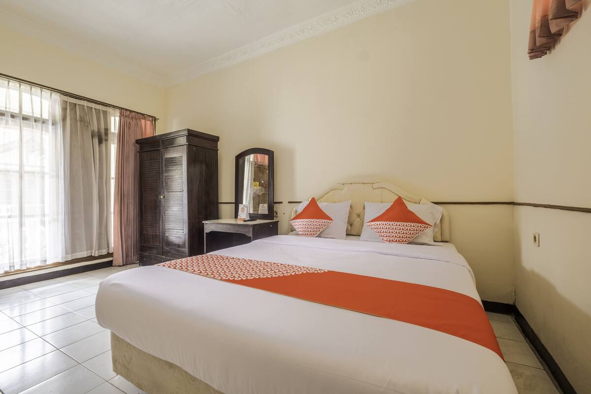 A hotel room with a large bed, a nightstand, a mirror, and a wardrobe.