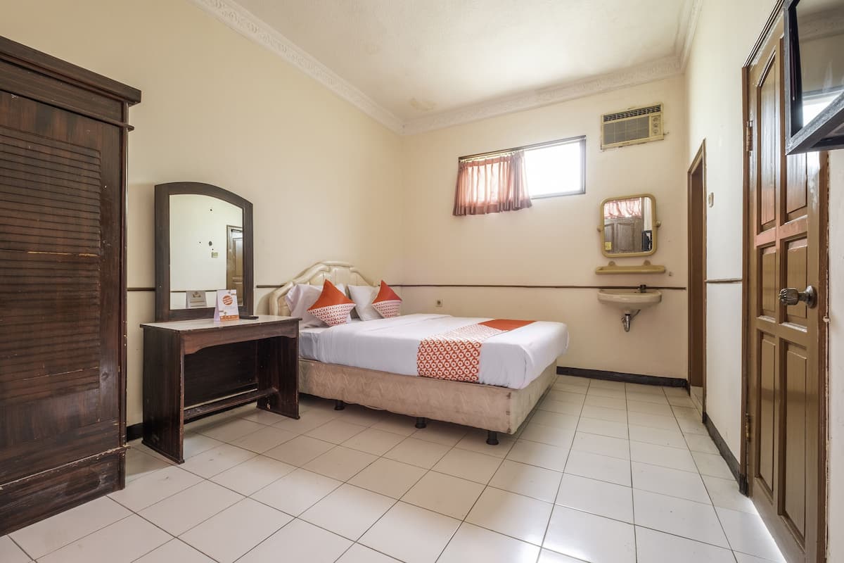 A bedroom with a bed, a dresser, a mirror, a window with curtains, a sink, and a door.