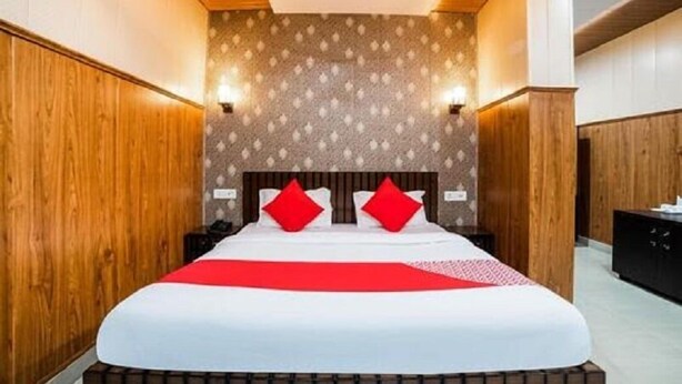 A modern hotel room with a wooden headboard, a patterned wall, and a red accent on the bed. - Krazy Hotel (Haldwani)