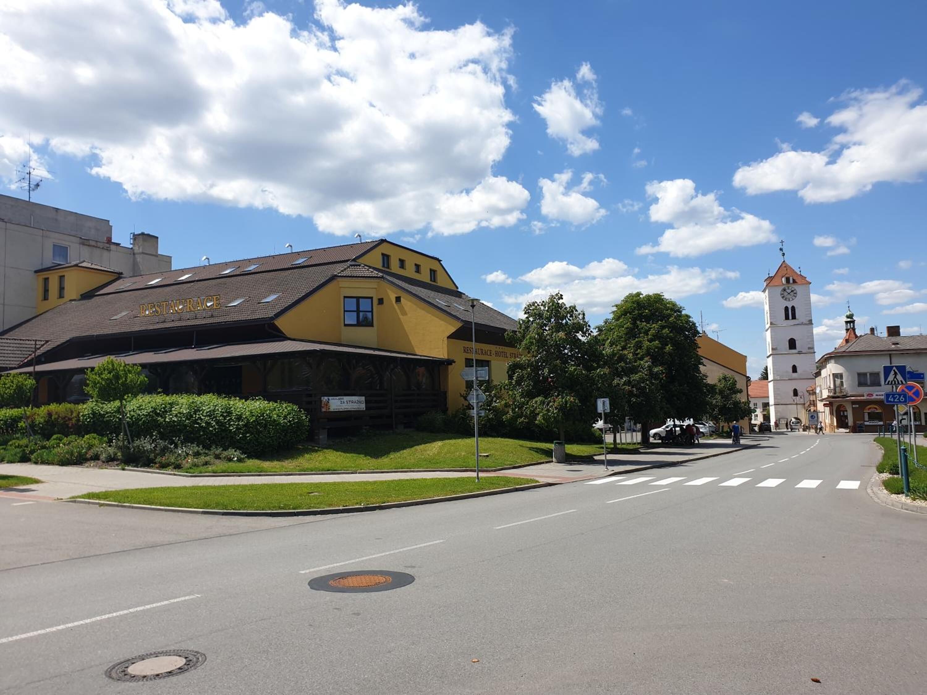 Un edificio amarillo con un cartel que dice "RESTAURACE HOTEL STRAUS" y una torre del reloj al fondo.