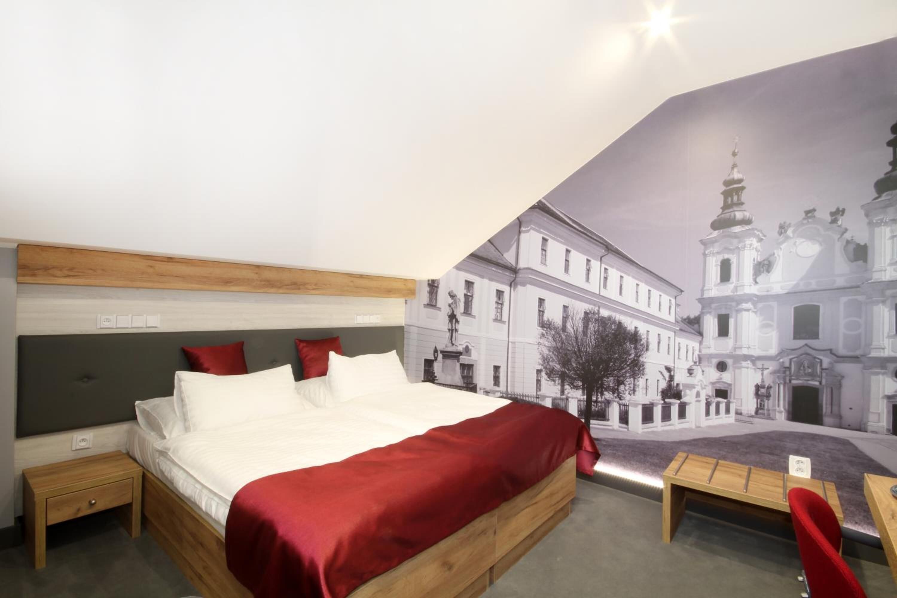 Una habitación de hotel con una cama, mesitas de noche, una silla roja y un mural de un edificio.