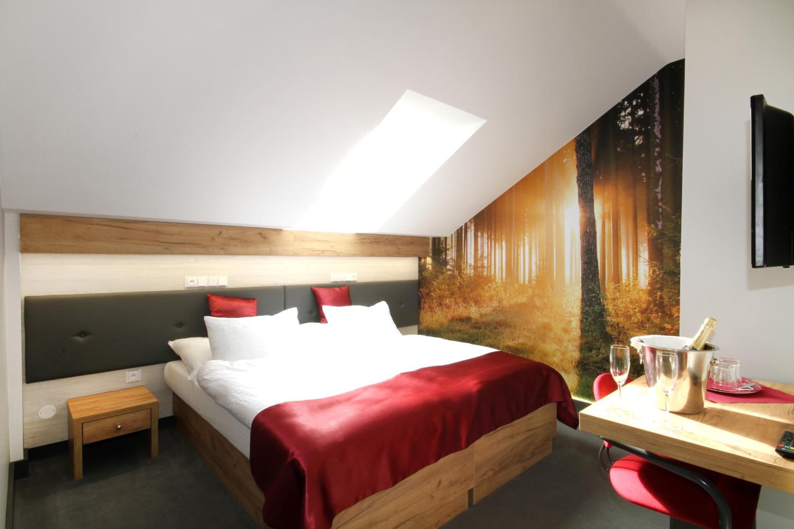 A modern bedroom with a skylight, a large bed, a desk with a chair, and a wall mural.