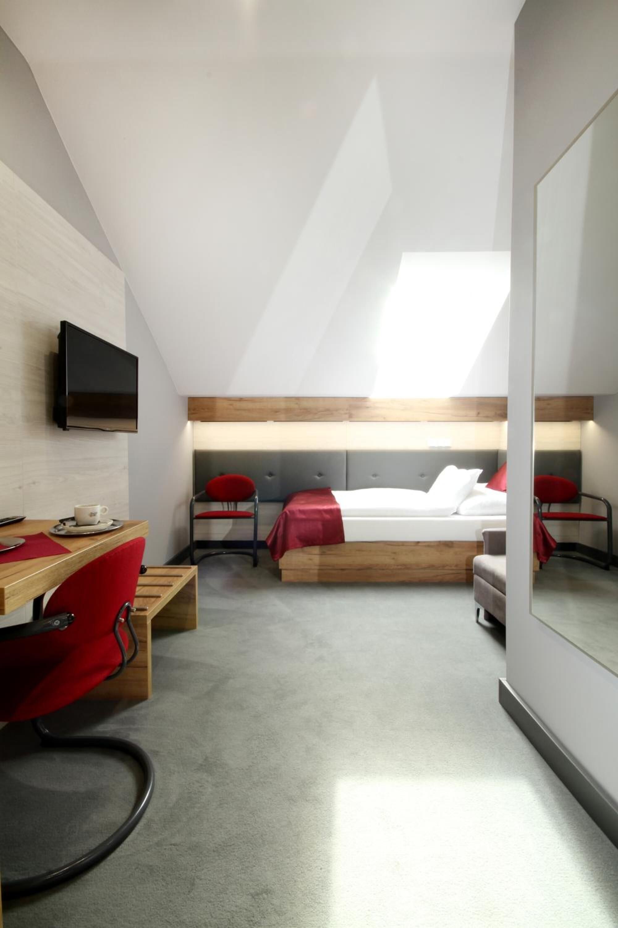 A modern hotel room with a loft bed, a desk with a chair, a television, and a large mirror.