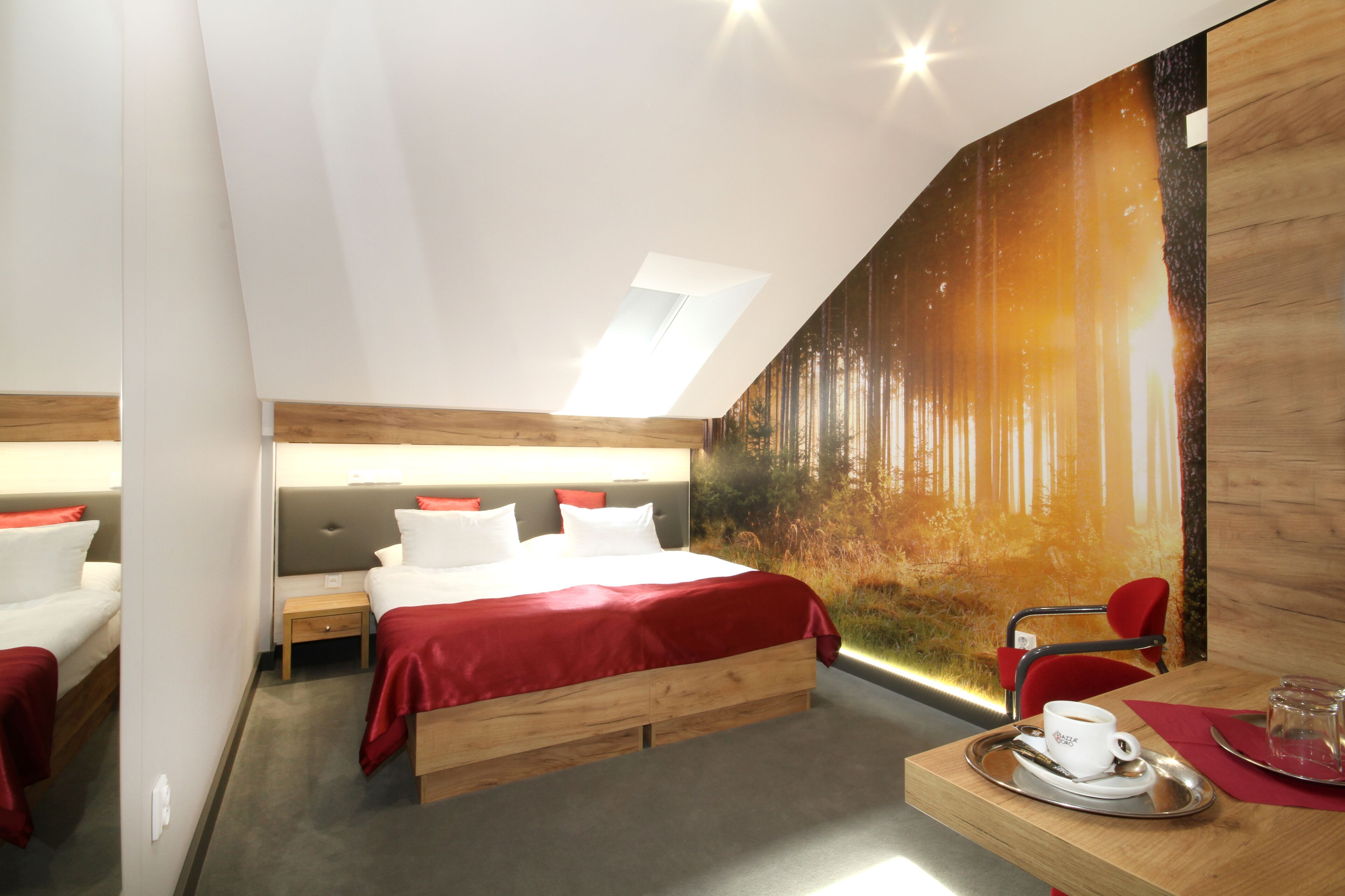 A modern hotel room with a large bed, a desk with a cup and saucer, and a mural of a forest scene.