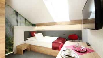A modern hotel room with a bed, a small desk with a cup of coffee, a red chair, and a TV.