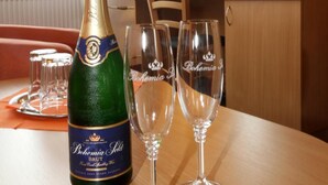 A bottle of Behemia Brut champagne and two champagne flutes on a wooden table in a hotel room. - Hotel Strážnice (Straznice)