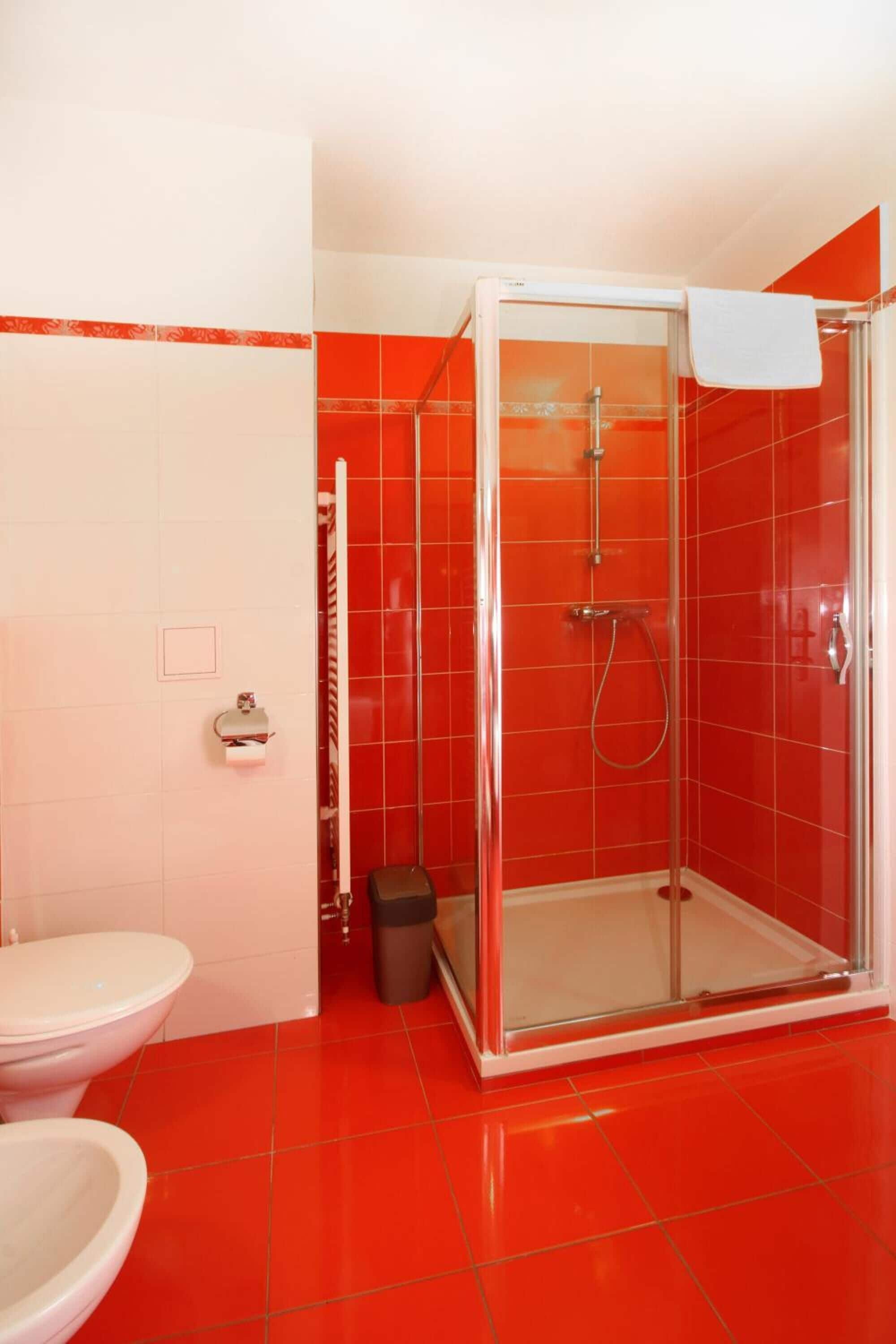 A bathroom with a glass-enclosed shower, a white toilet, and a trash bin.