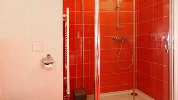 A bathroom with a glass-enclosed shower, a white toilet, and a trash bin.