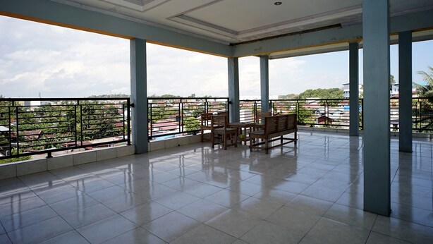 A spacious balcony with tiled flooring and wooden furniture, overlooking a residential area with greenery and buildings. - OYO 2343 Winolanto Guest House Syariah (Balikpapan)