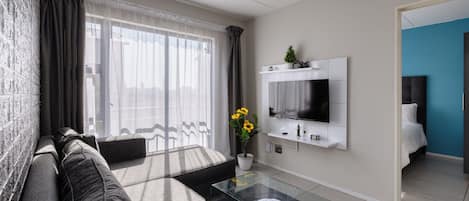 Un salon moderne avec un canapé, une table basse en verre, un téléviseur fixé au mur et une plante en pot.
