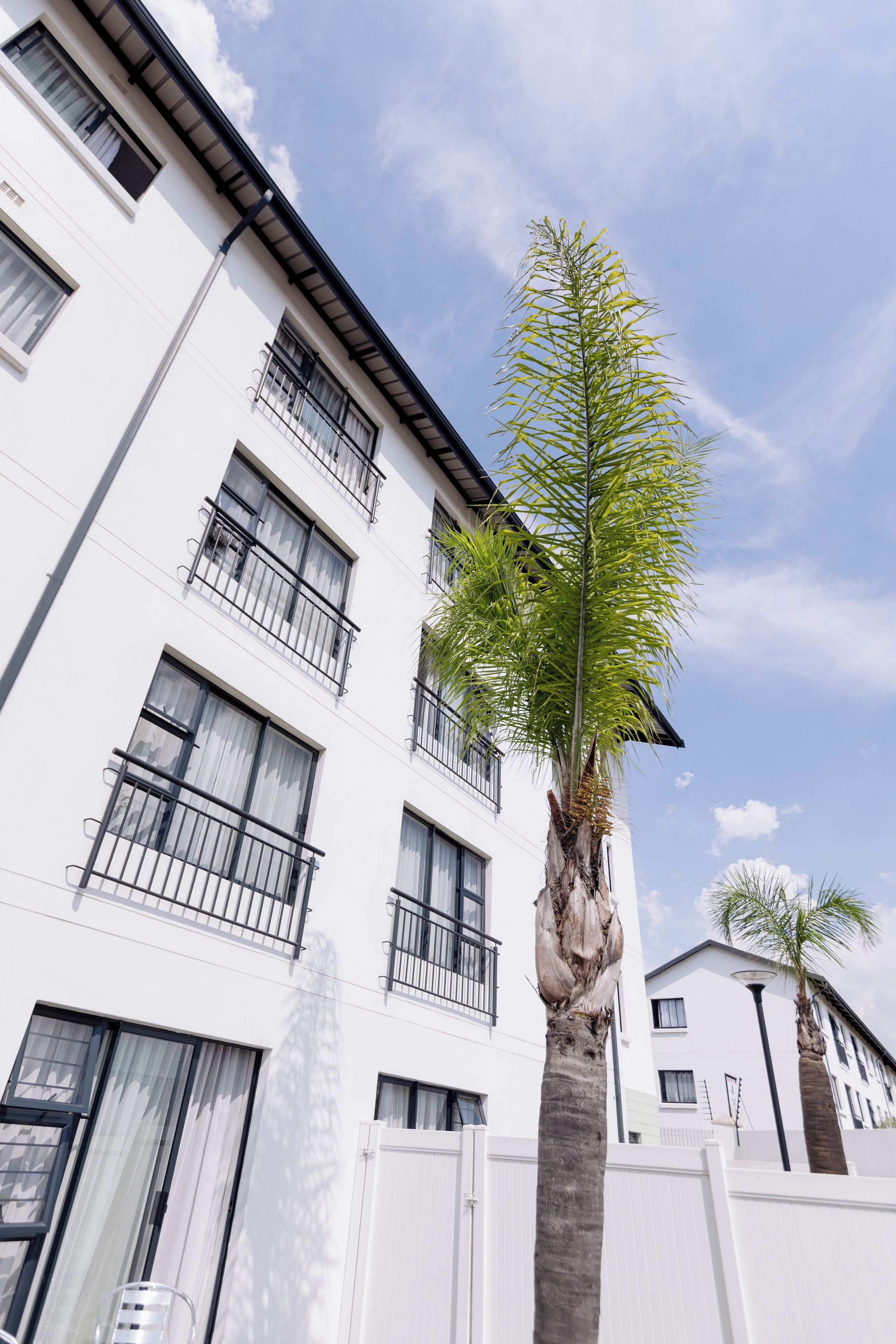 Ein mehrstöckiges Gebäude mit Balkonen, einer Palme und blauem Himmel.
