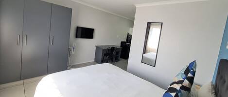 Habitación de hotel con cama, escritorio, silla, televisor y armario.