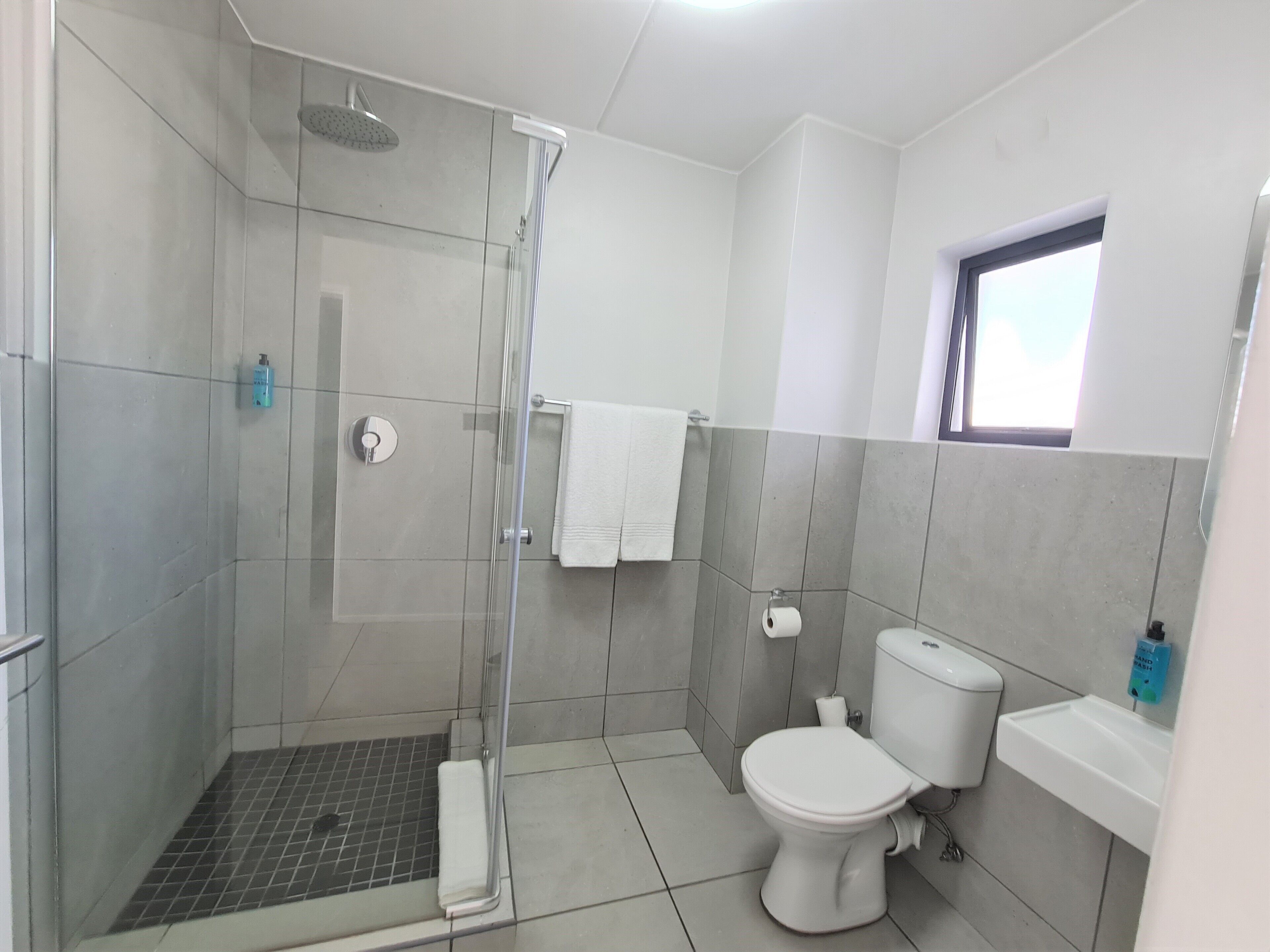 Un baño moderno con ducha de mampara de vidrio, inodoro y lavamanos.