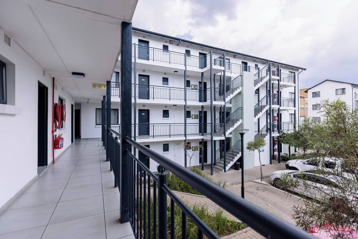 A multi-story residential building with balconies, a covered walkway, and a parking area.