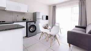 A modern kitchen with a washing machine, a dining table with chairs, and a gray sofa. - MINT Express Sandton View (Sandton)
