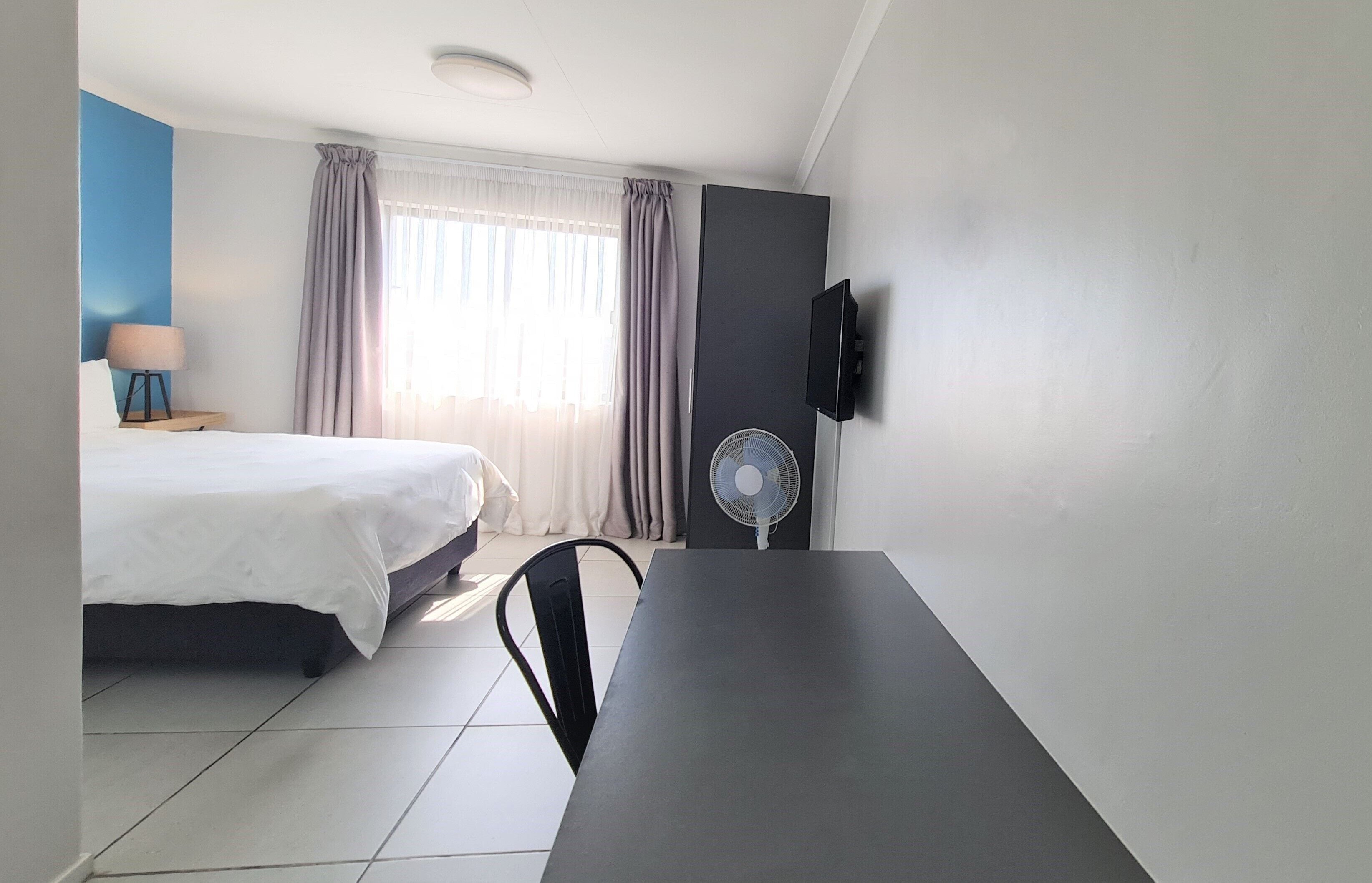 Une chambre d’hôtel équipée d’un lit, d’un bureau, d’une chaise, d’une télévision, d’un ventilateur et de rideaux.