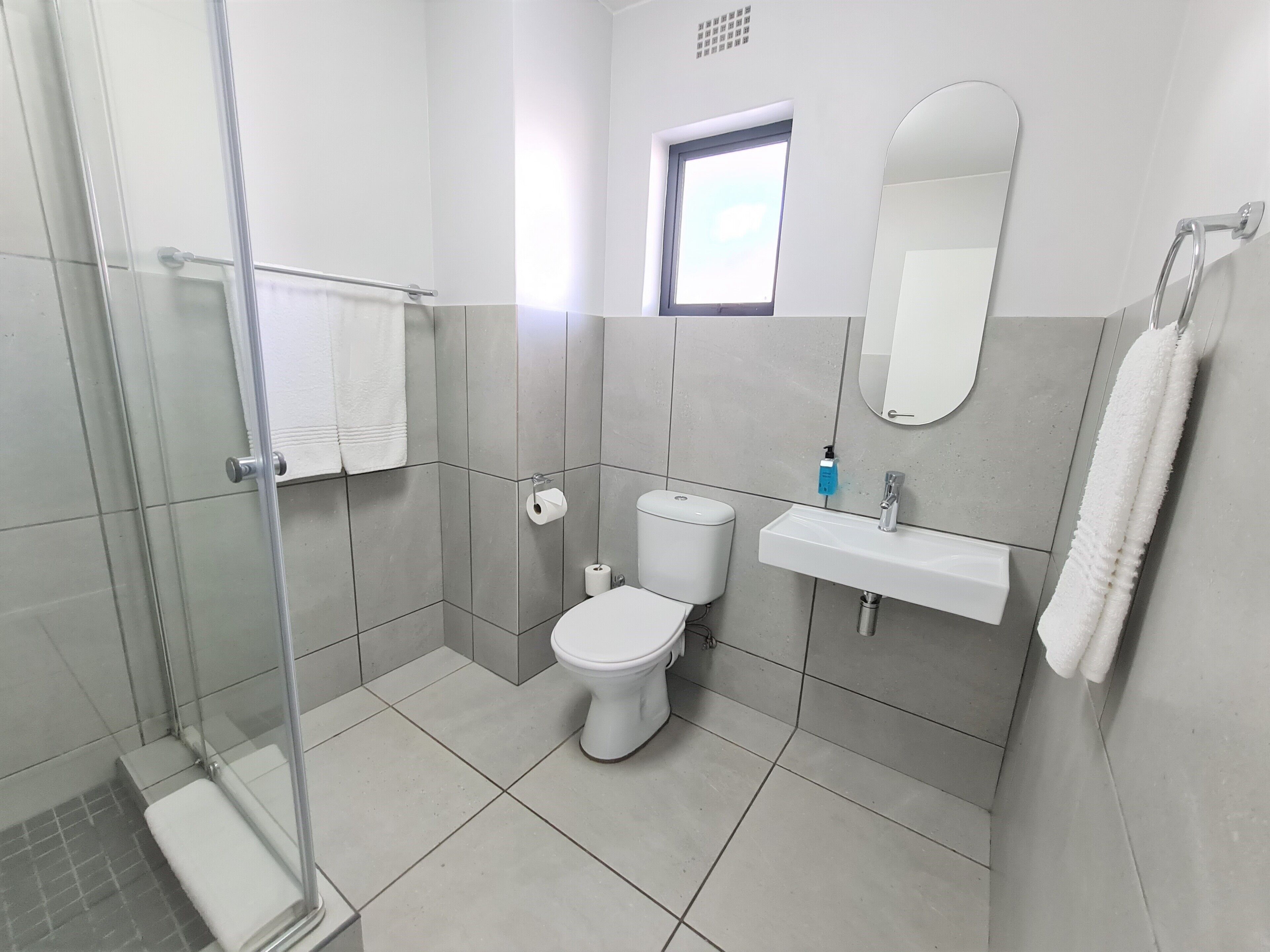 Un baño moderno con cabina de ducha de vidrio, inodoro, lavamanos y espejo.