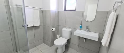 Un baño moderno con cabina de ducha de vidrio, inodoro, lavamanos y espejo.