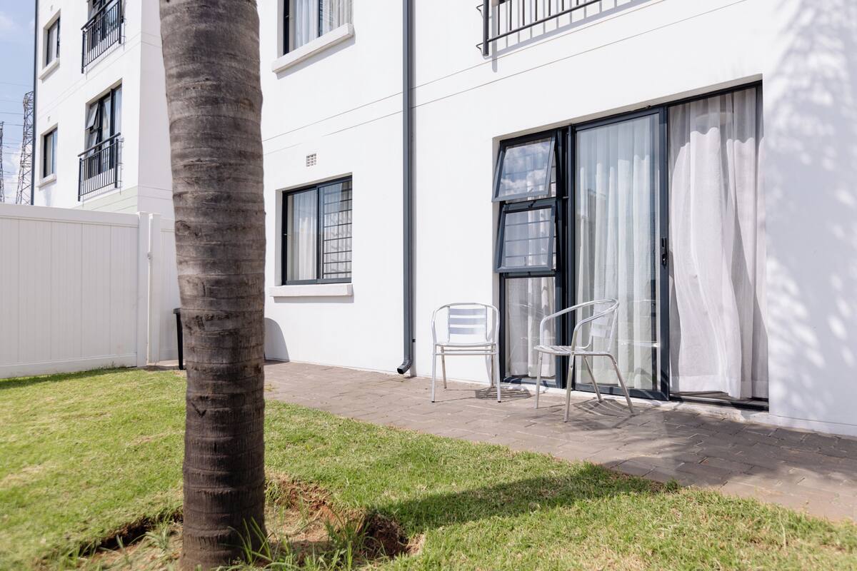 A white building with a balcony, a palm tree, and two chairs.