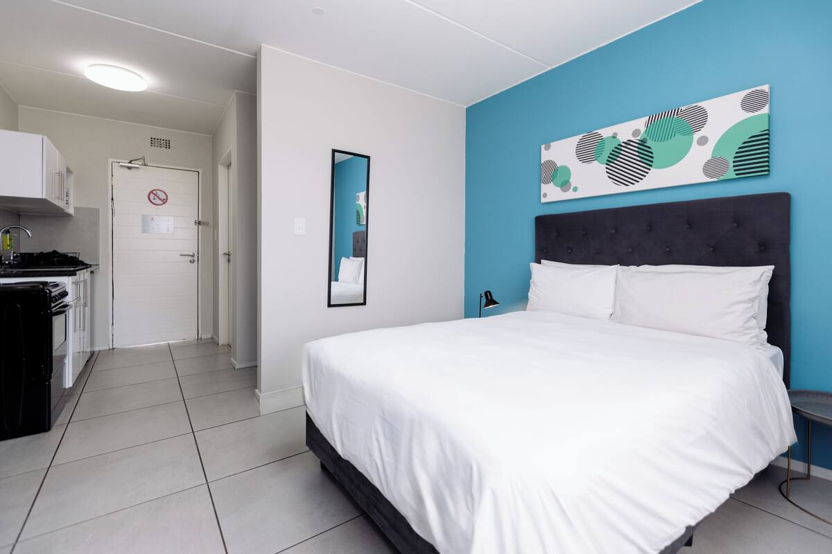 A bedroom with a bed, a mirror, a wall art piece, and a door with a no-smoking sign.