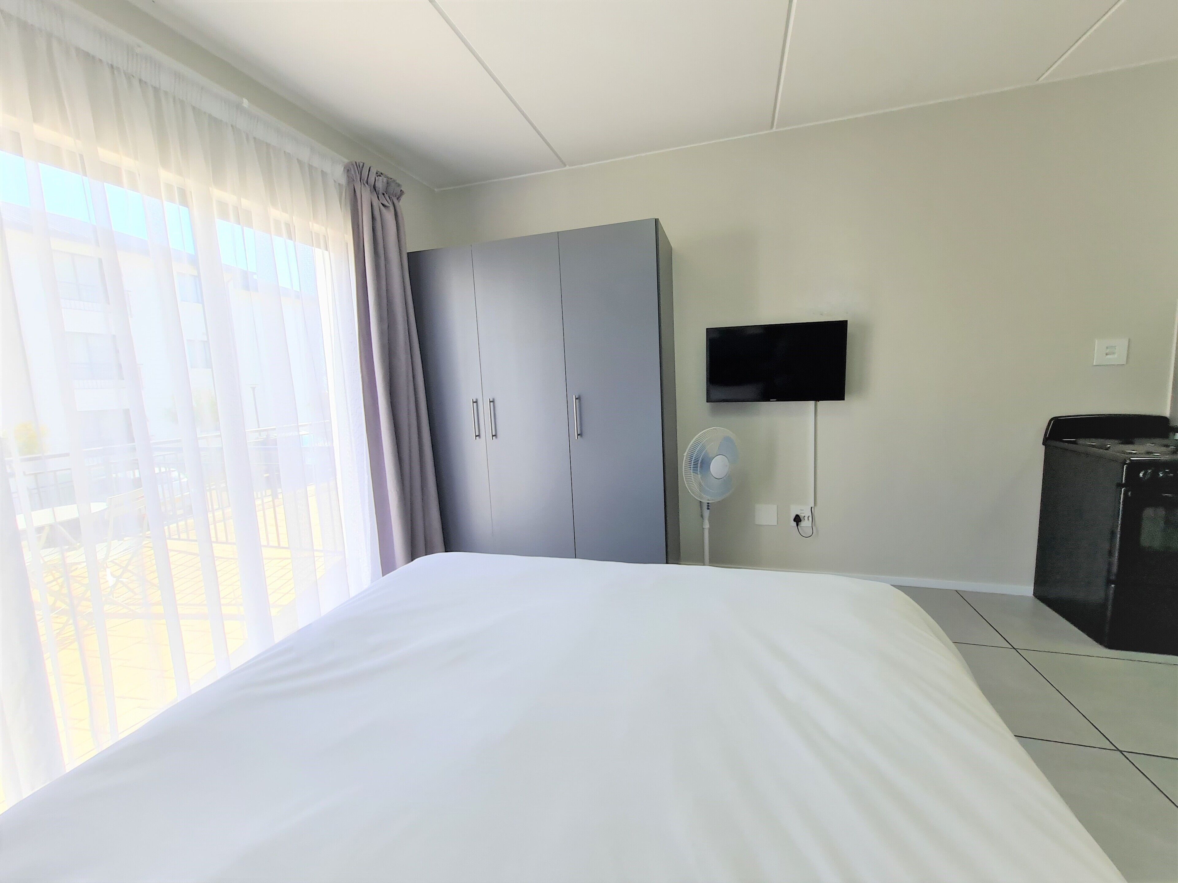 Una camera d'albergo con un letto, un armadio, una televisione a parete e una ventola.