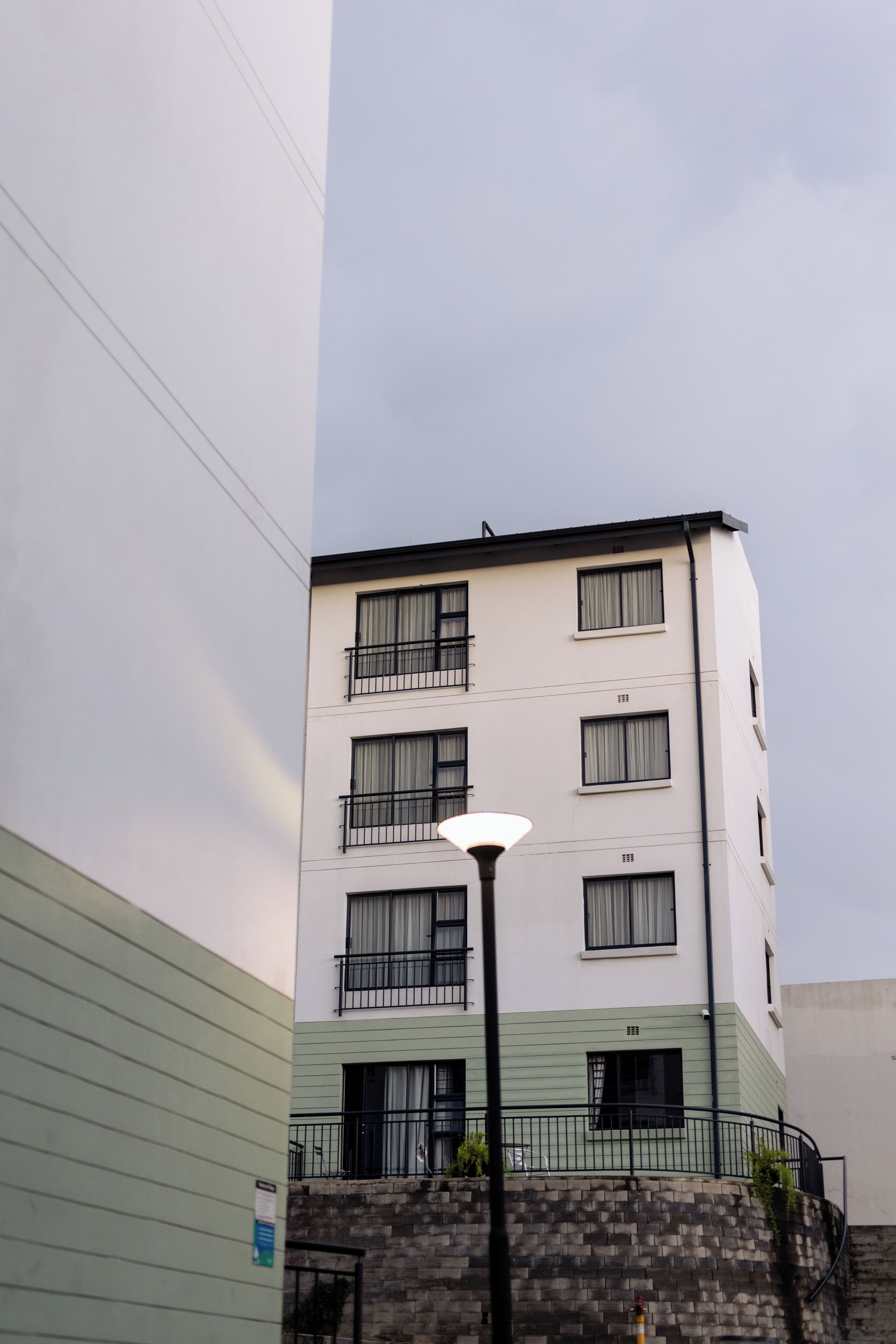 Un edificio de varios pisos con balcones, una farola y un muro de ladrillo.