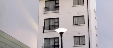 Un edificio de varios pisos con balcones, una farola y un muro de ladrillo.
