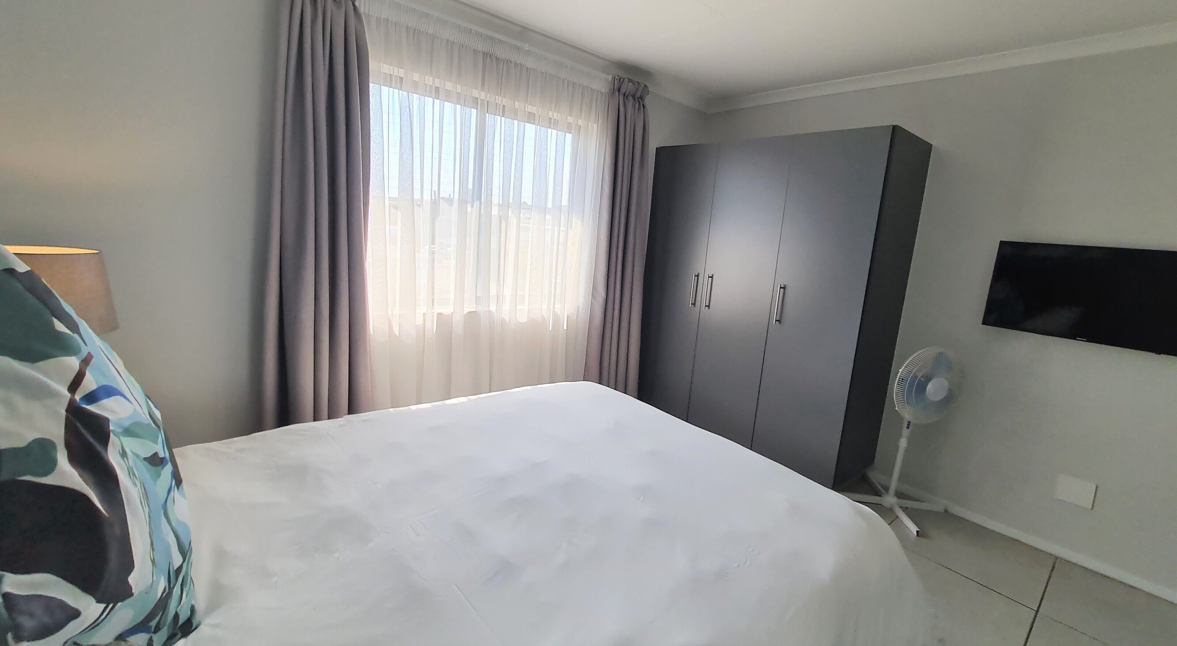 A bedroom with a bed, a wardrobe, a TV, and a fan.