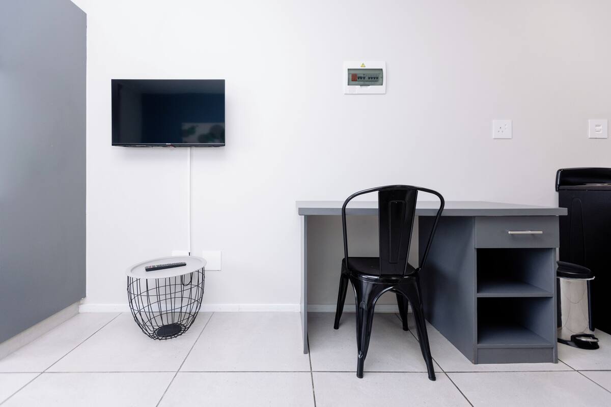 A modern room with a desk, chair, TV, and a small trash bin.