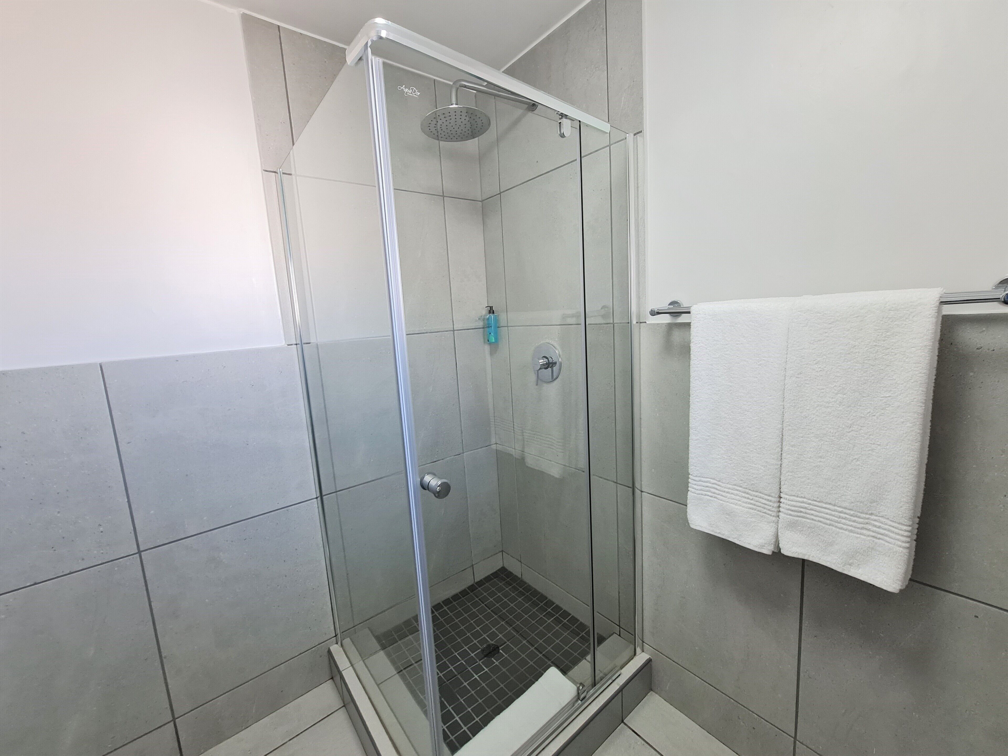 Um chuveiro com paredes de vidro, um chuveiro manual e uma toalha branca pendurada em um suporte, com paredes revestidas de azulejos.