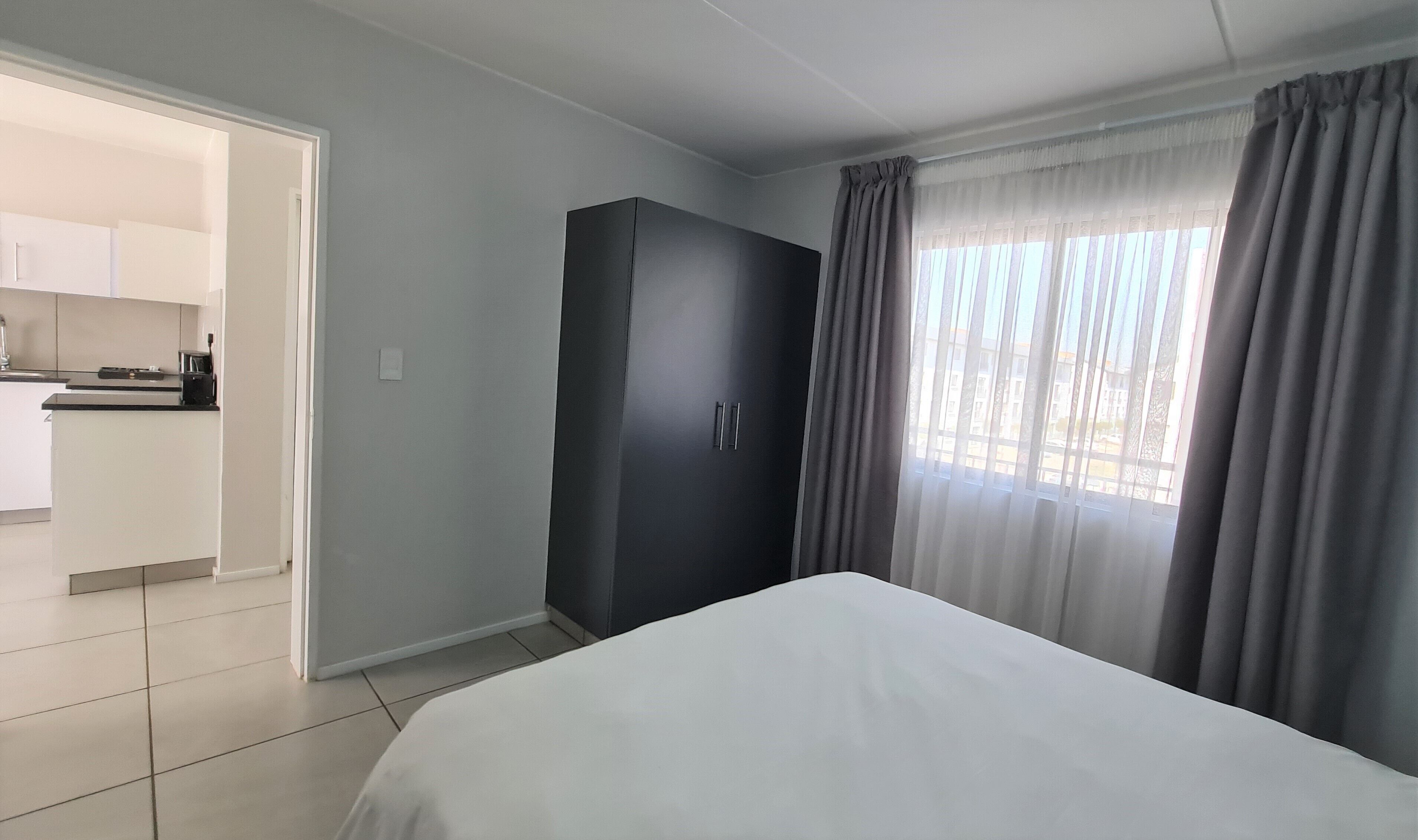 Une chambre d’hôtel comprenant un lit, une armoire, un coin cuisine et une fenêtre avec des rideaux.