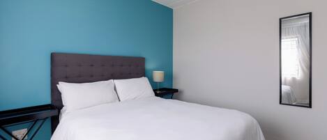 A neatly made bed with white linens, a dark headboard, and a small bedside table with a lamp.
