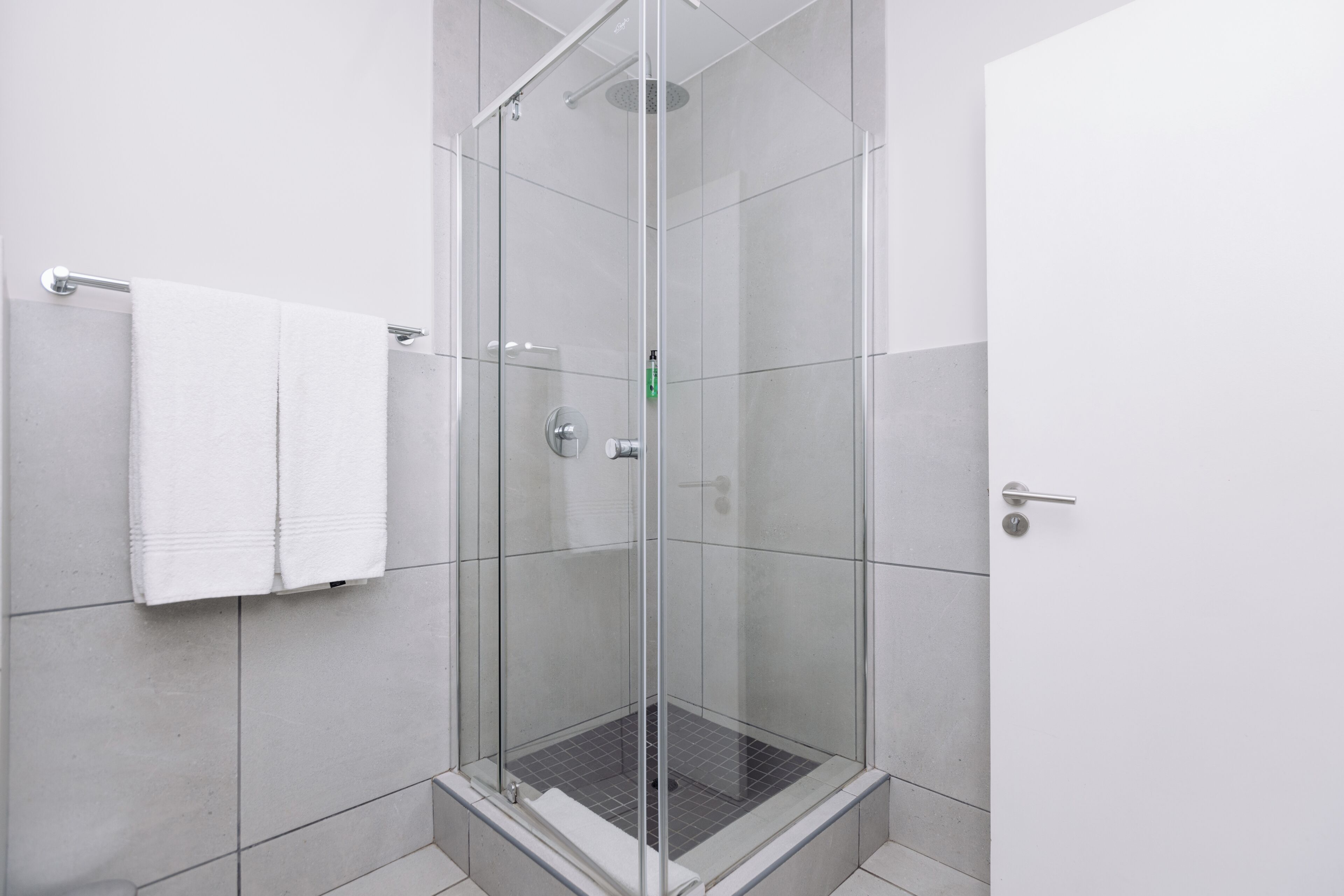 Una ducha con paredes de vidrio, piso de cerámica, un perchero y una puerta.