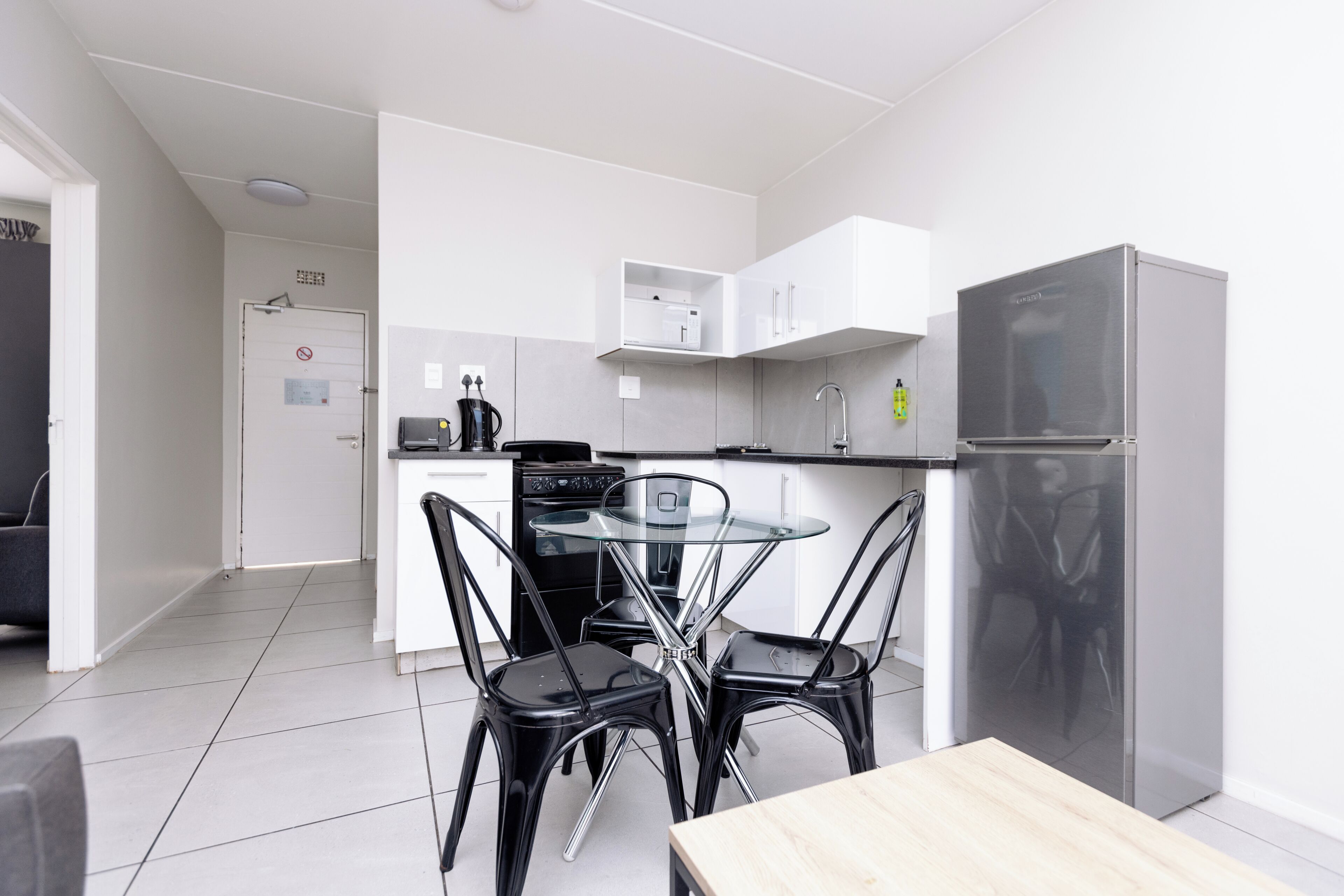 Una cocina moderna con armarios blancos, una mesa de comedor de vidrio y sillas negras.