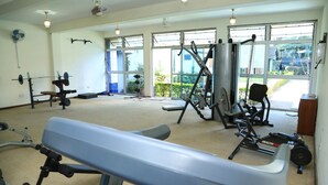 A gym with various exercise equipment, large windows, and a ceiling fan. - Hillview Apartments (Kampala)
