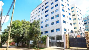 A multi-story building with a tiled facade, a gated entrance, and a clear sky. - Hillview Apartments (Kampala)
