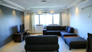 A modern living room with a sectional sofa, a flat-screen TV, and a coffee table. - Hillview Apartments (Kampala)