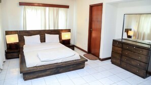 A bedroom with a wooden bed, two bedside tables with lamps, a dresser, and a door. - Hillview Apartments (Kampala)