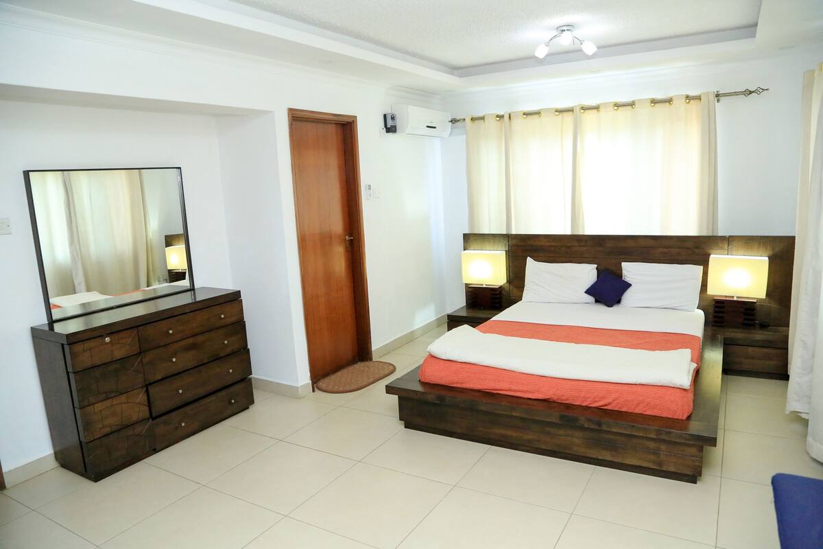 A bedroom with a bed, bedside lamps, a dresser, a mirror, and a door.