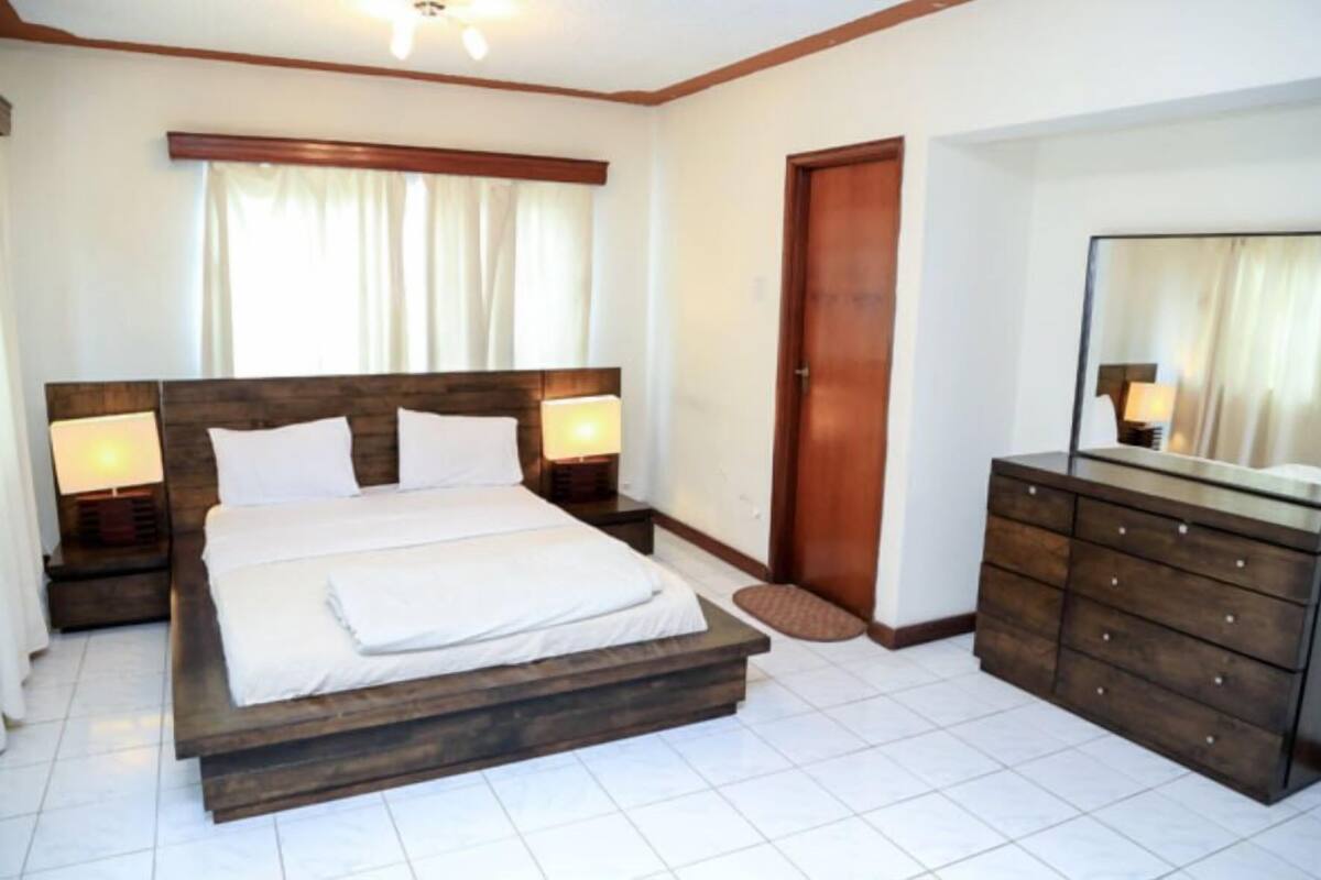 A bedroom with a wooden bed, bedside lamps, a dresser, and a door.
