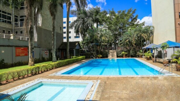 A swimming pool area with two pools, surrounded by palm trees and a building in the background. - Hillview Apartments (Kampala)
