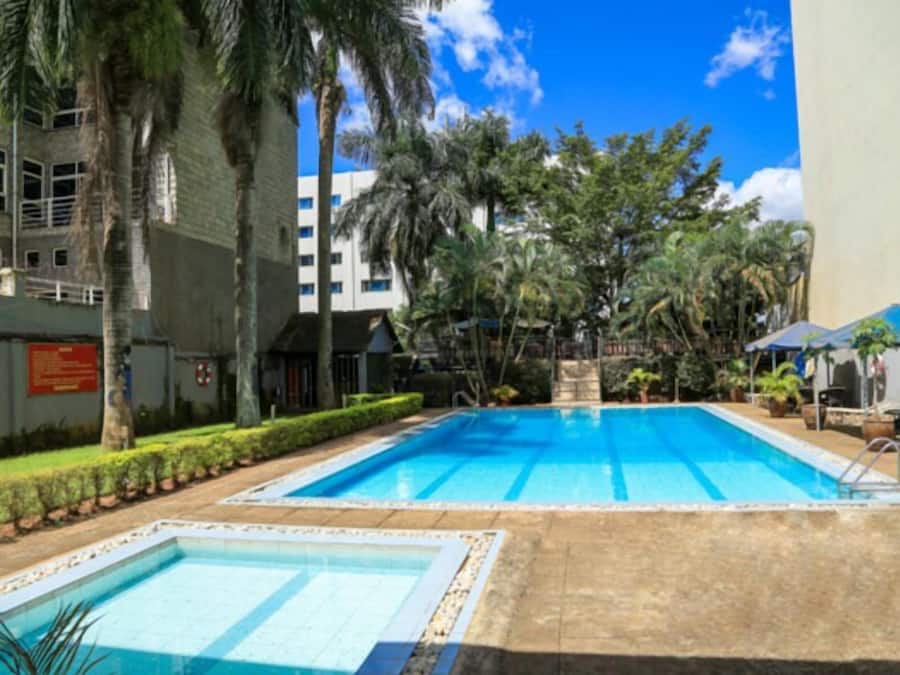 Zona de piscina con dos piscinas, rodeada de palmeras y un edificio al fondo.