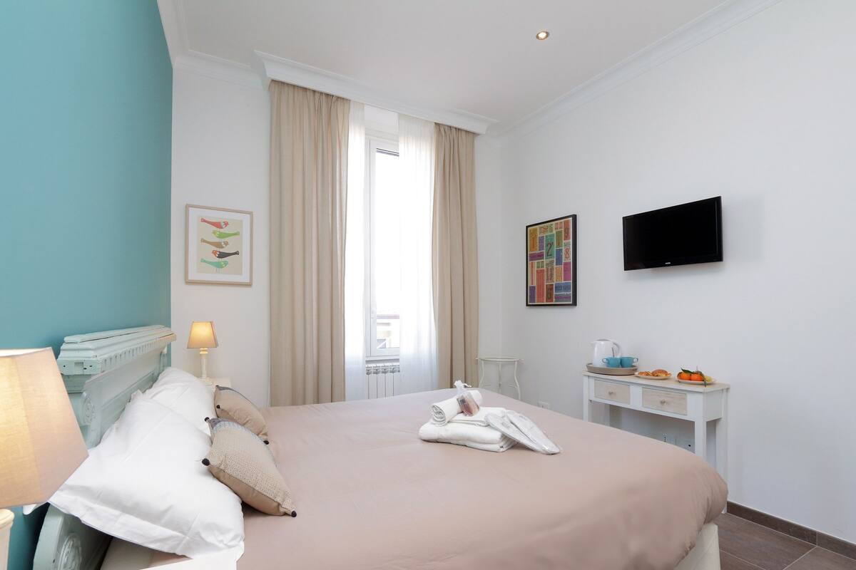 Ein Hotelzimmer mit Bett, Fernseher, Schreibtisch mit Kaffeemaschine und einem Fenster mit Vorhängen.