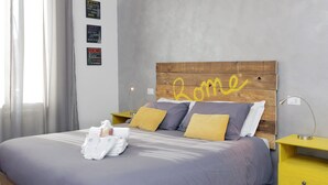 Uma cama bem arrumada com cabeceira de madeira, duas mesas de cabeceira e uma parede com três placas.