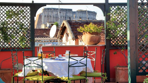 Um terraço com uma mesa posta para refeições, um vaso de planta e vista para um edifício histórico.