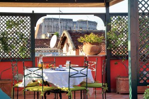 A terrace with a table set for dining, a potted plant, and a view of a historic building. - B & B Li Rioni (Rome)