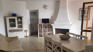 A living room with a sofa, dining table, chairs, a TV, a fireplace, and a cabinet. - Sea view apartment with FREE PARKING in the courtyard 30 meters from the sea on OFFER (Cala Gonone)