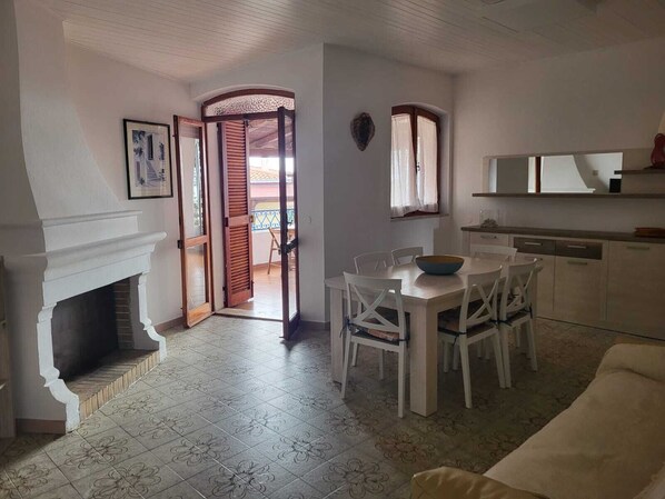 A dining area with a white table and chairs, a fireplace, and a view through an open door to a balcony.