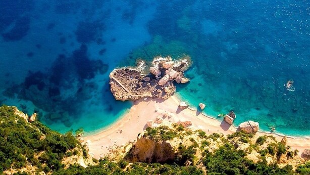 An aerial view of a coastal area with clear turquoise waters, rocky formations, and a sandy beach. - Sea view apartment with FREE PARKING in the courtyard 30 meters from the sea on OFFER (Cala Gonone)