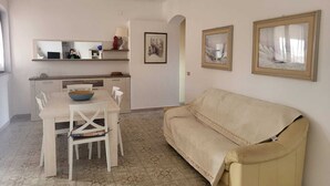 A dining area with a table and chairs, a sofa, and a kitchen area with a counter and shelves. - Sea view apartment with FREE PARKING in the courtyard 30 meters from the sea on OFFER (Cala Gonone)